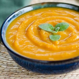 Butternut squash soup garnished with sage leaves in blue bowl