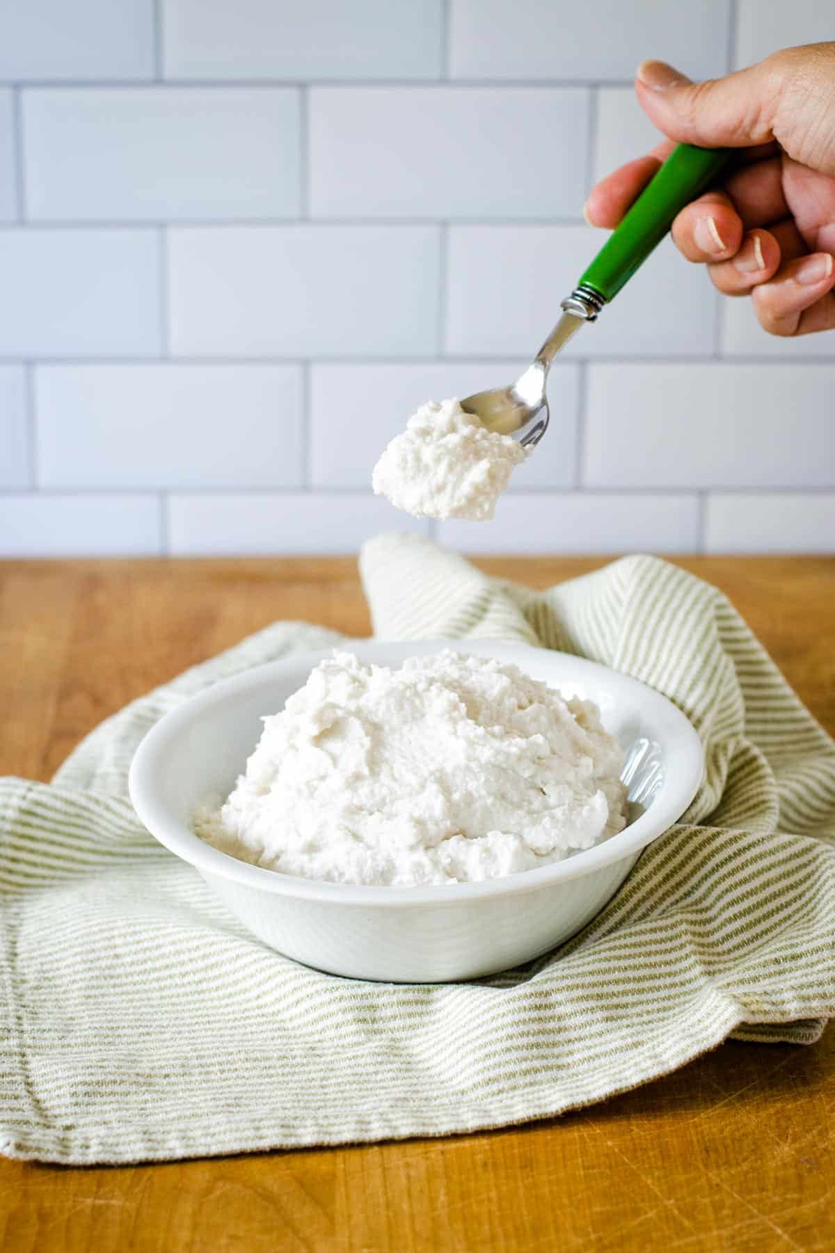 Bowl of coconut milk whipped cream with hand scooping out a spoonful