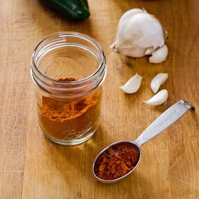 Homemade chili powder in mason jar and spoon with head of garlic