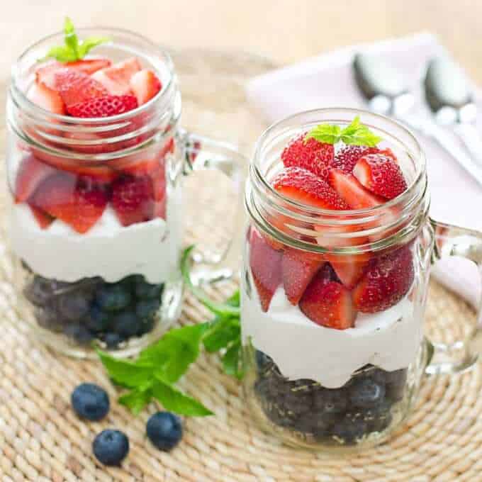 Fresh summer strawberries, whipped coconut cream, and blueberries layered in a tall glass mug for a red, white an blue dessert