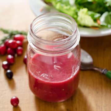 Cranberry salad dressing in mason jar next to cranberries, spoon and lettuce.