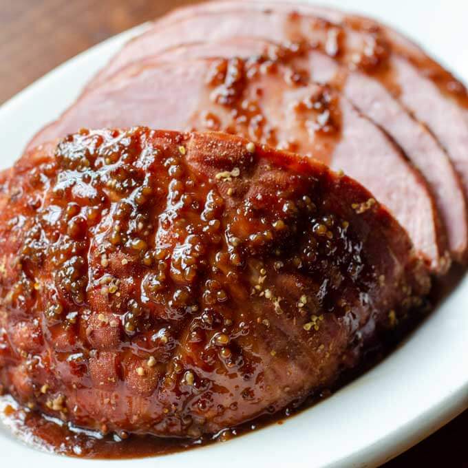 Ham with honey mustard pomegranate glaze on white platter.