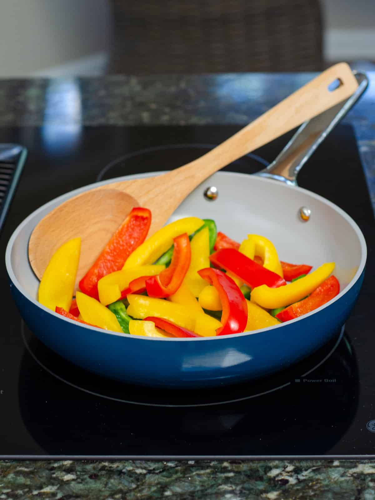 Blue fry pan with peppers on stove.