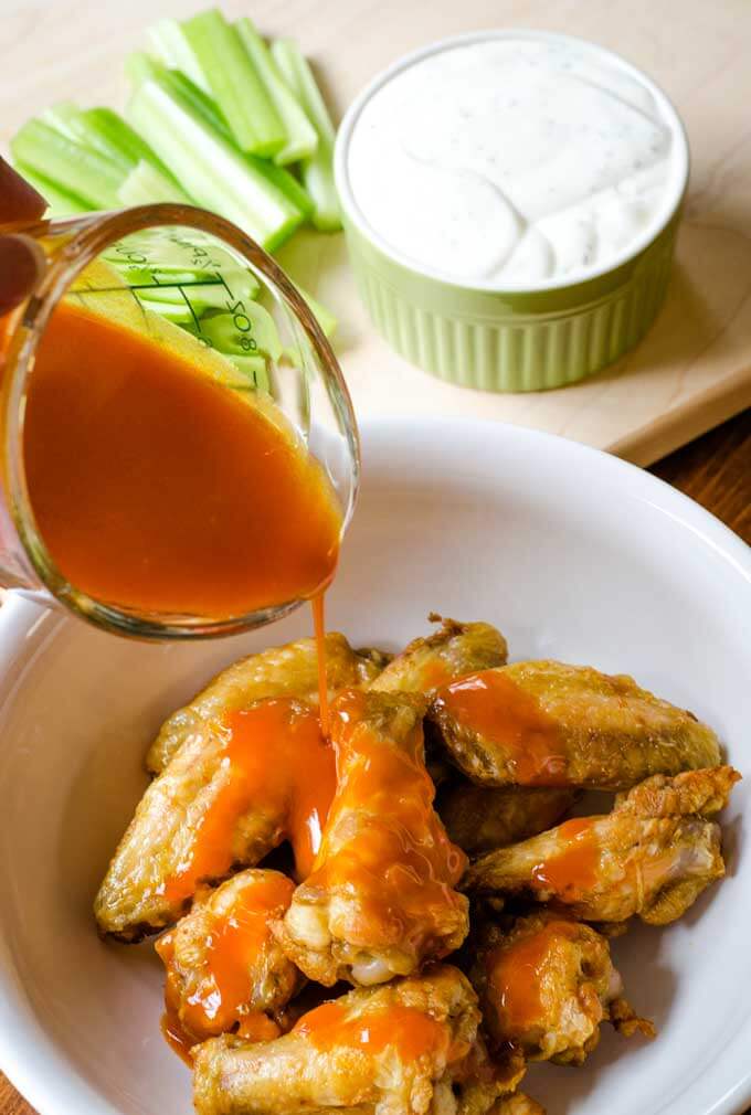 Pouring Buffalo sauce over air fryer chicken wings