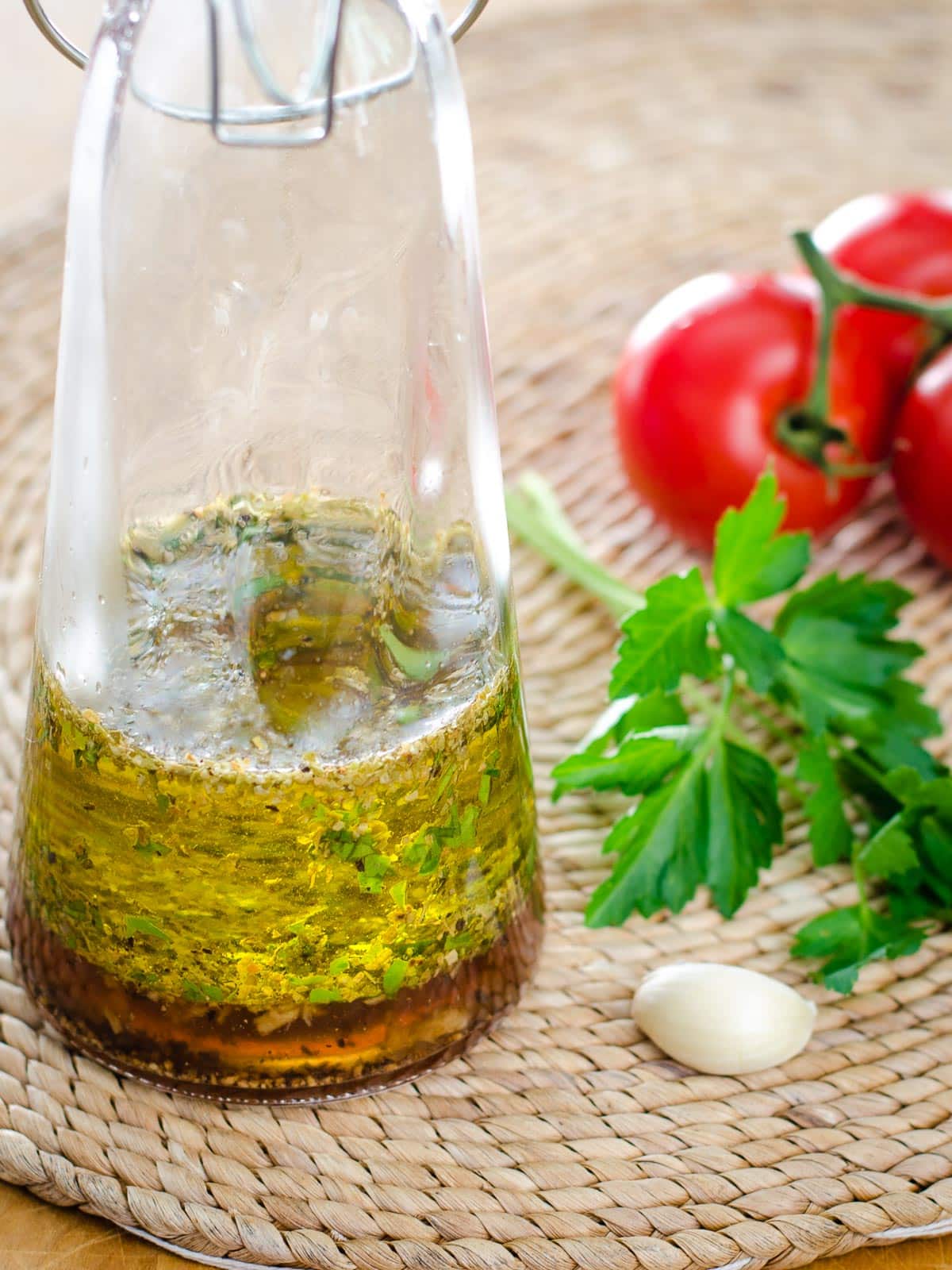 Italian dressing in glass bottle next to garlic, parsley and tomatoes