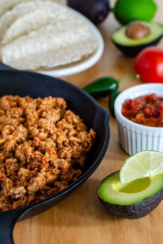 Taco meat in cast iron skillet, avocado, lime, salsa, taco shells