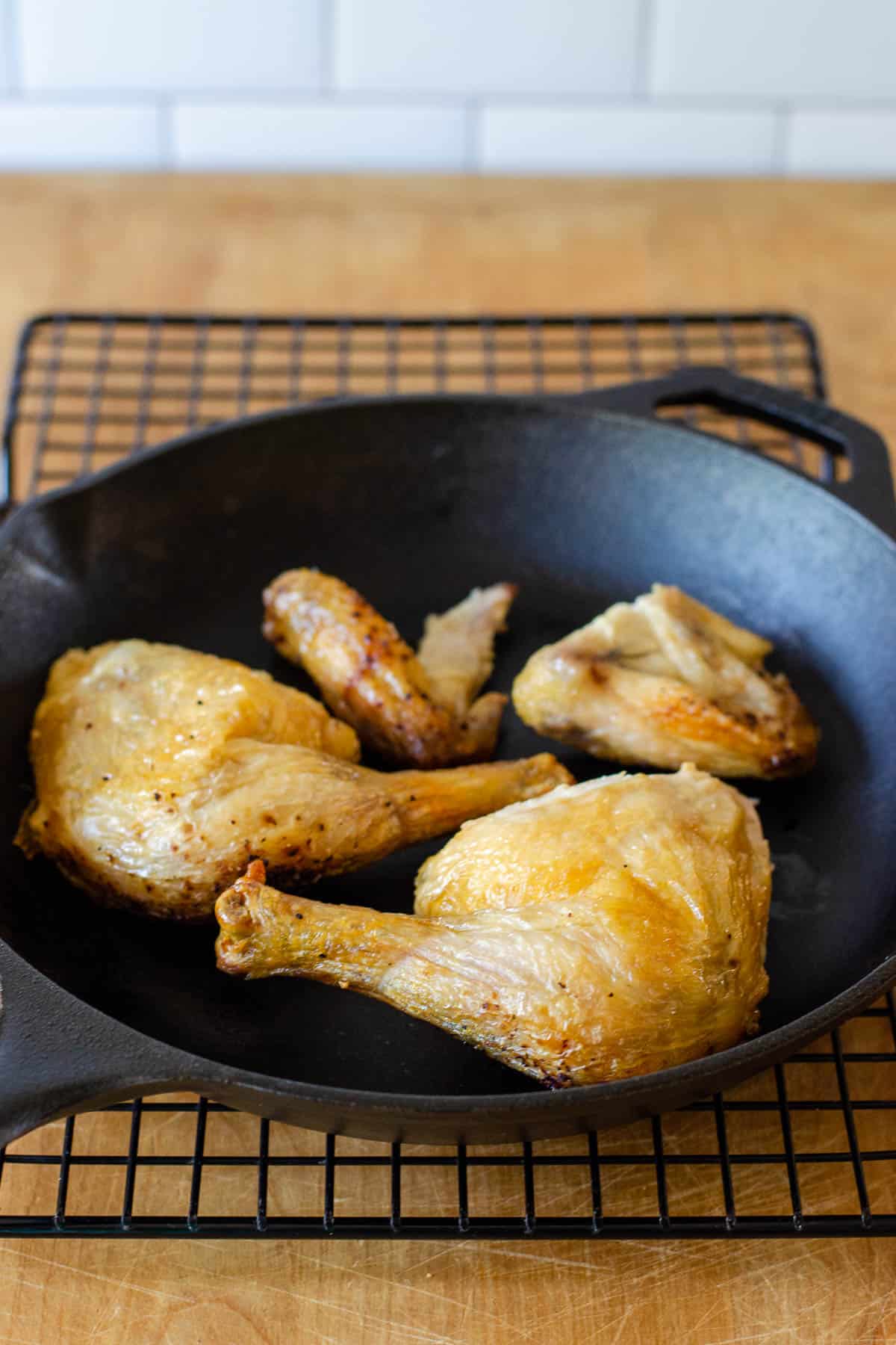 Chicken pieces in cast iron skillet on cooling rack