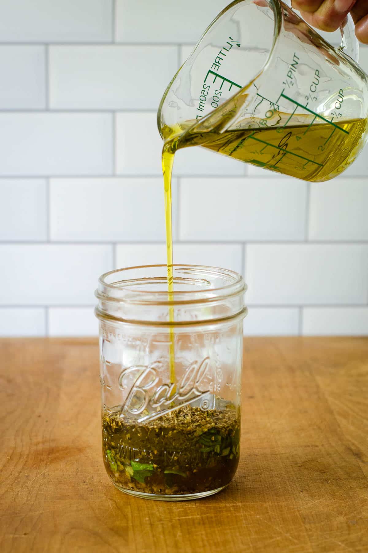 Pouring olive oil into mason jar with dressing ingredients