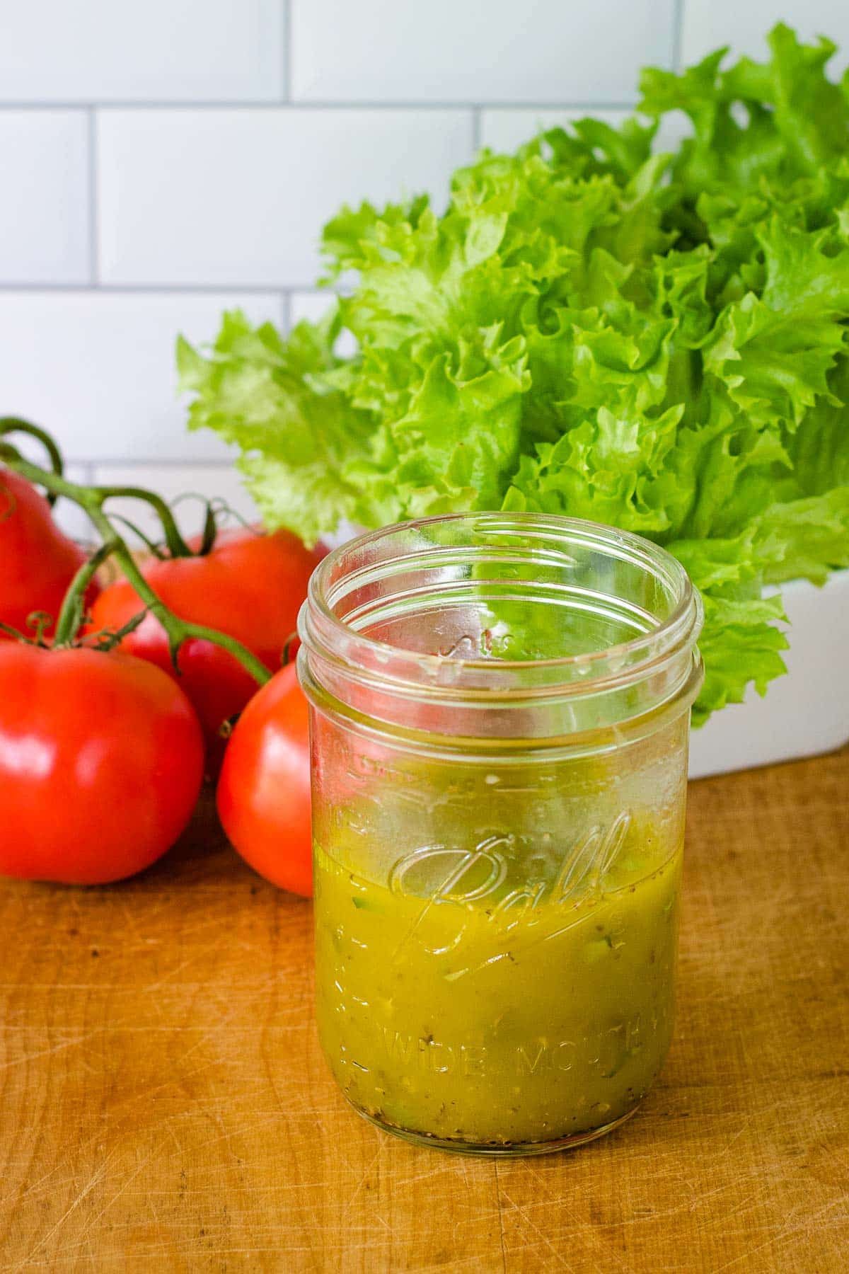 Italian dressing in mason jar next to tomatoes and lettuce