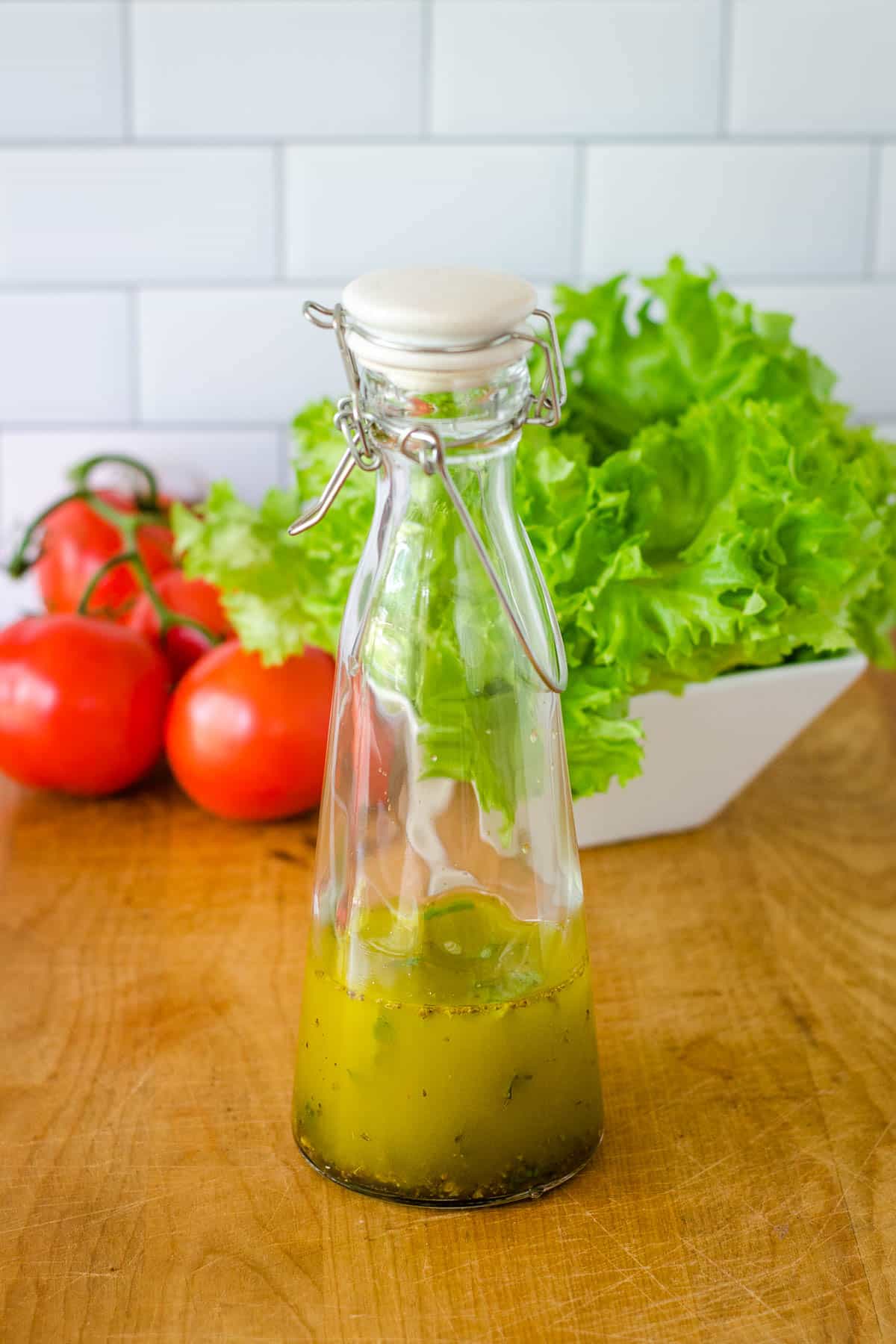 Homemade Italian dressing in glass botte in front of tomatoes and lettuce