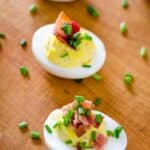 Deviled eggs with bacon and chives on cutting board.