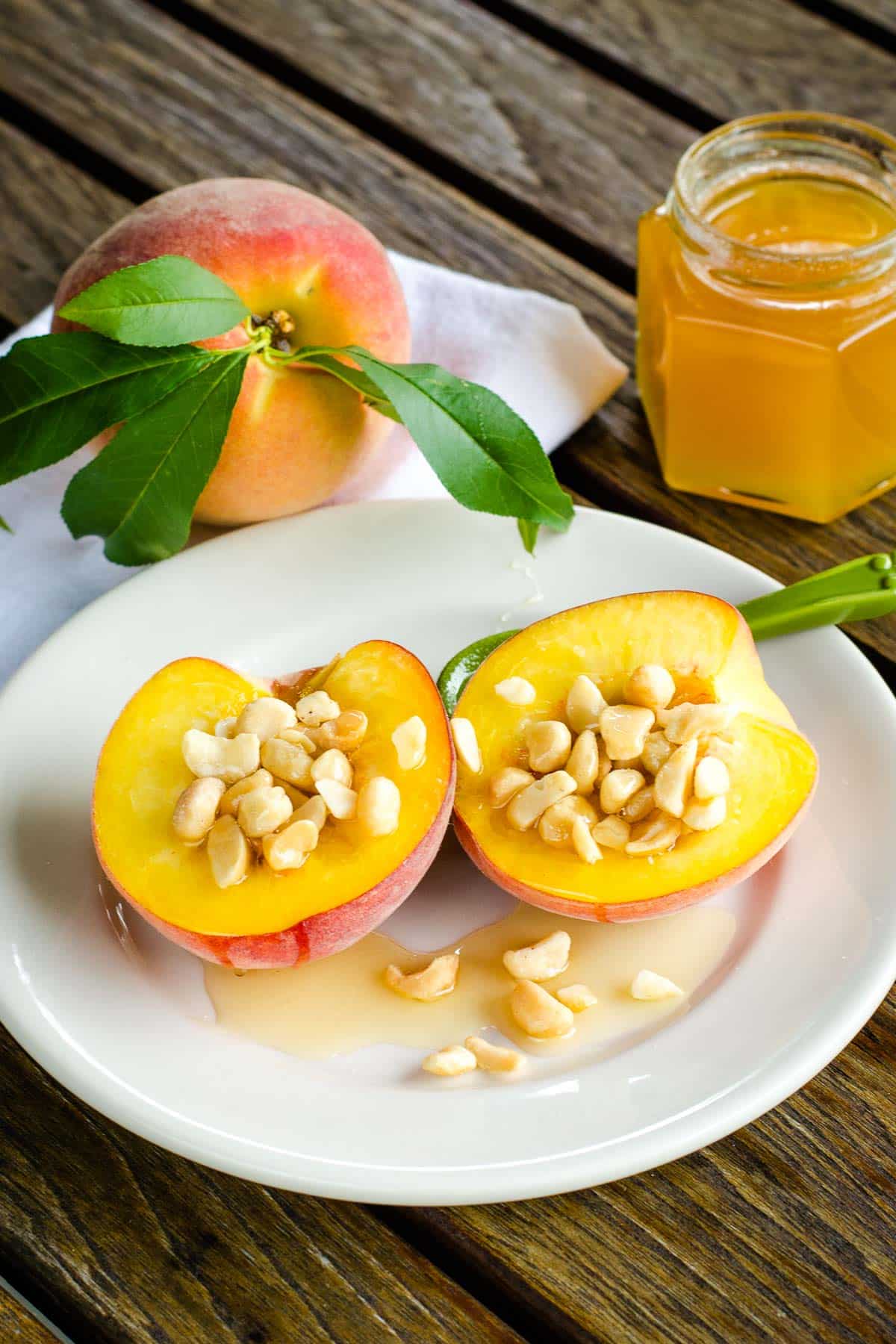 Peach halves with macadamia nuts and honey on white plate with whole peach and honey jar.