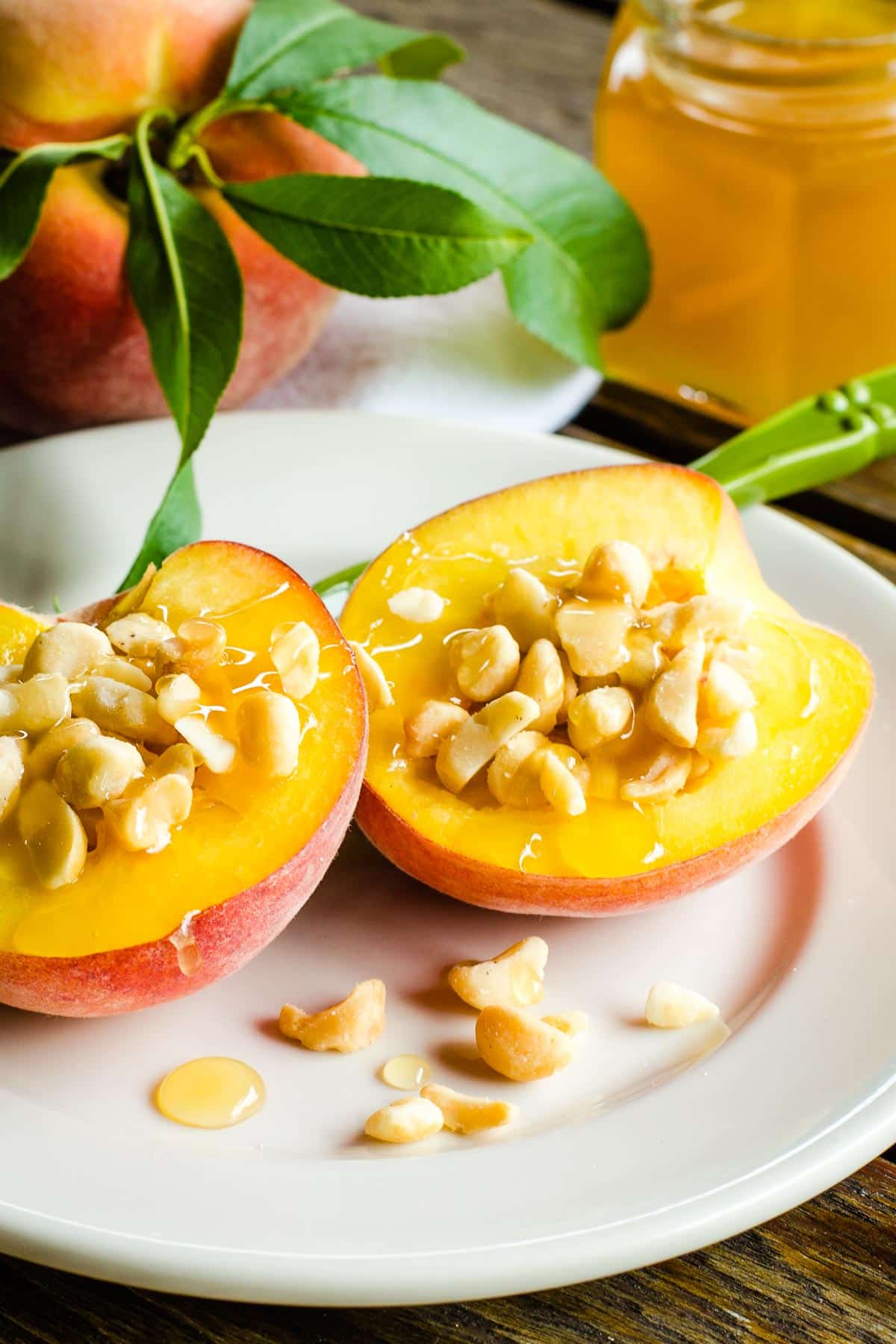Peaches with macadamia nuts and honey on white plate.