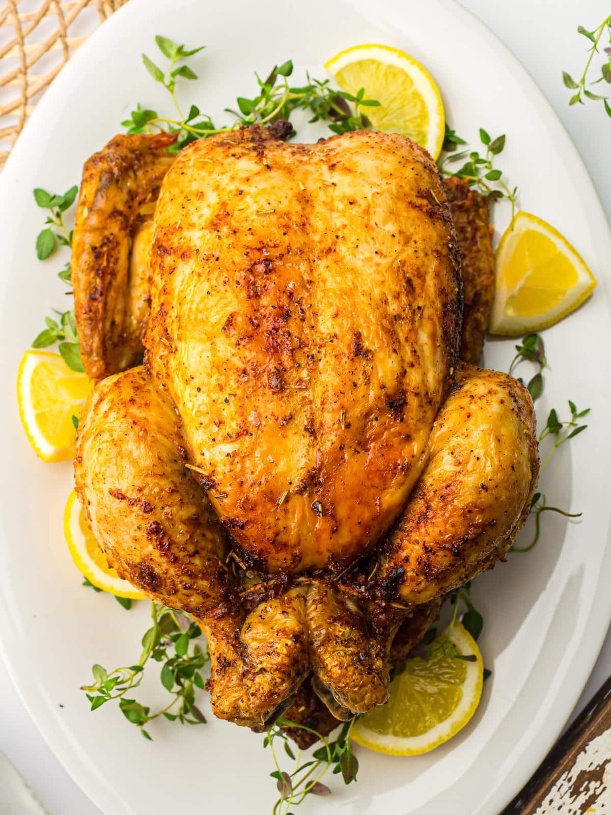 Cooked whole chicken on white platter with herbs and lemon.