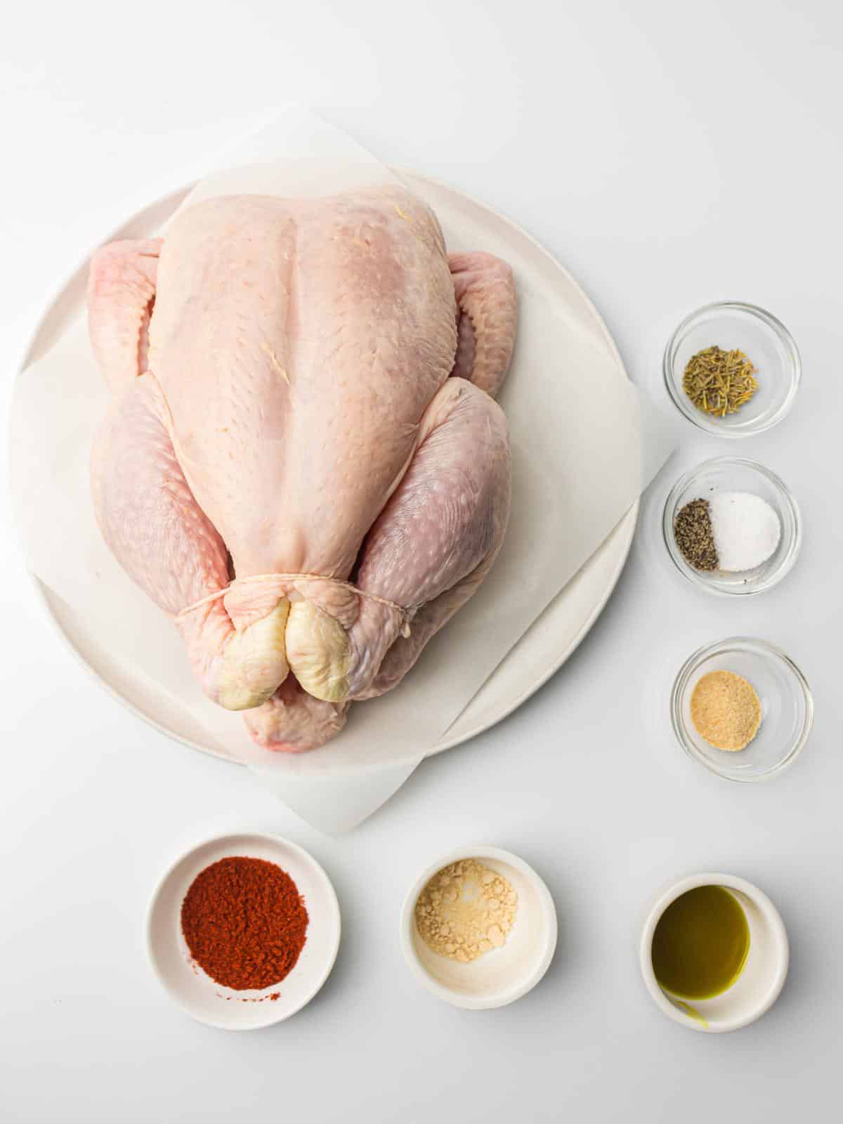 Raw chicken on plate next to bowls of spices and oil.