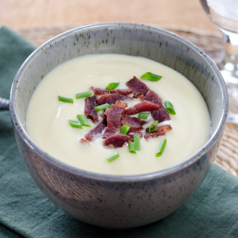 Cauliflower and celeriac soup topped with bacon and chives in ceramic bowl.