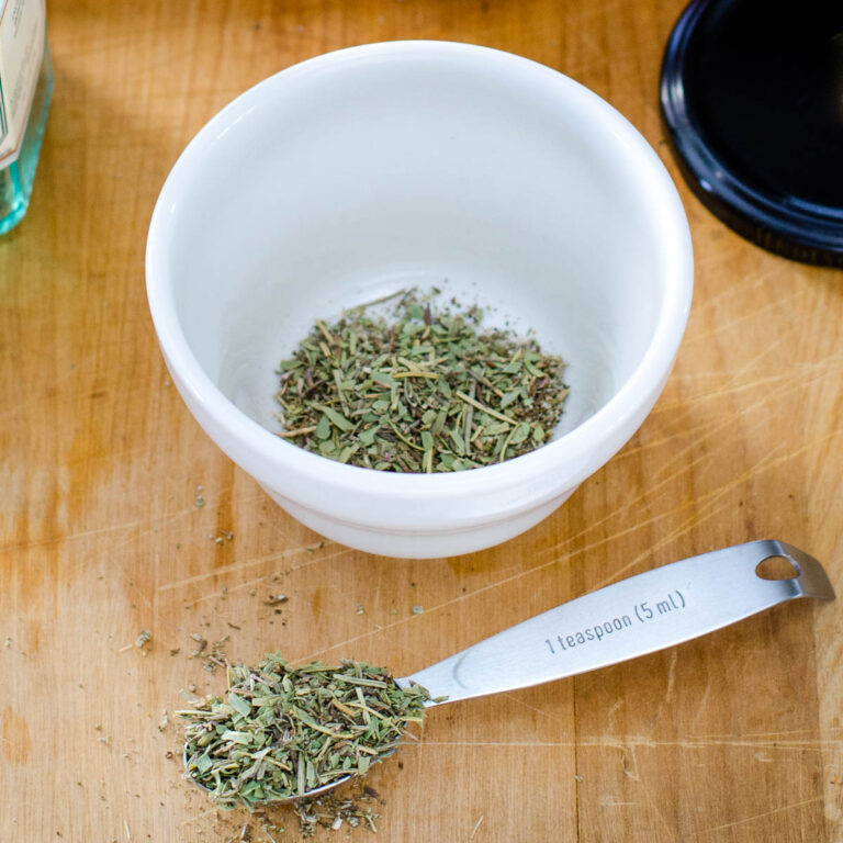 Spoonful of herbs de Provence in front of bowl with herb blend.