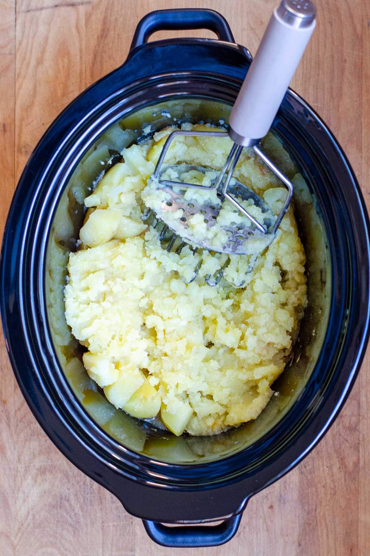 Potato masher in crock pot with mashed potatoes.