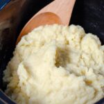 Mashed potatoes with wooden spoon in crock pot.