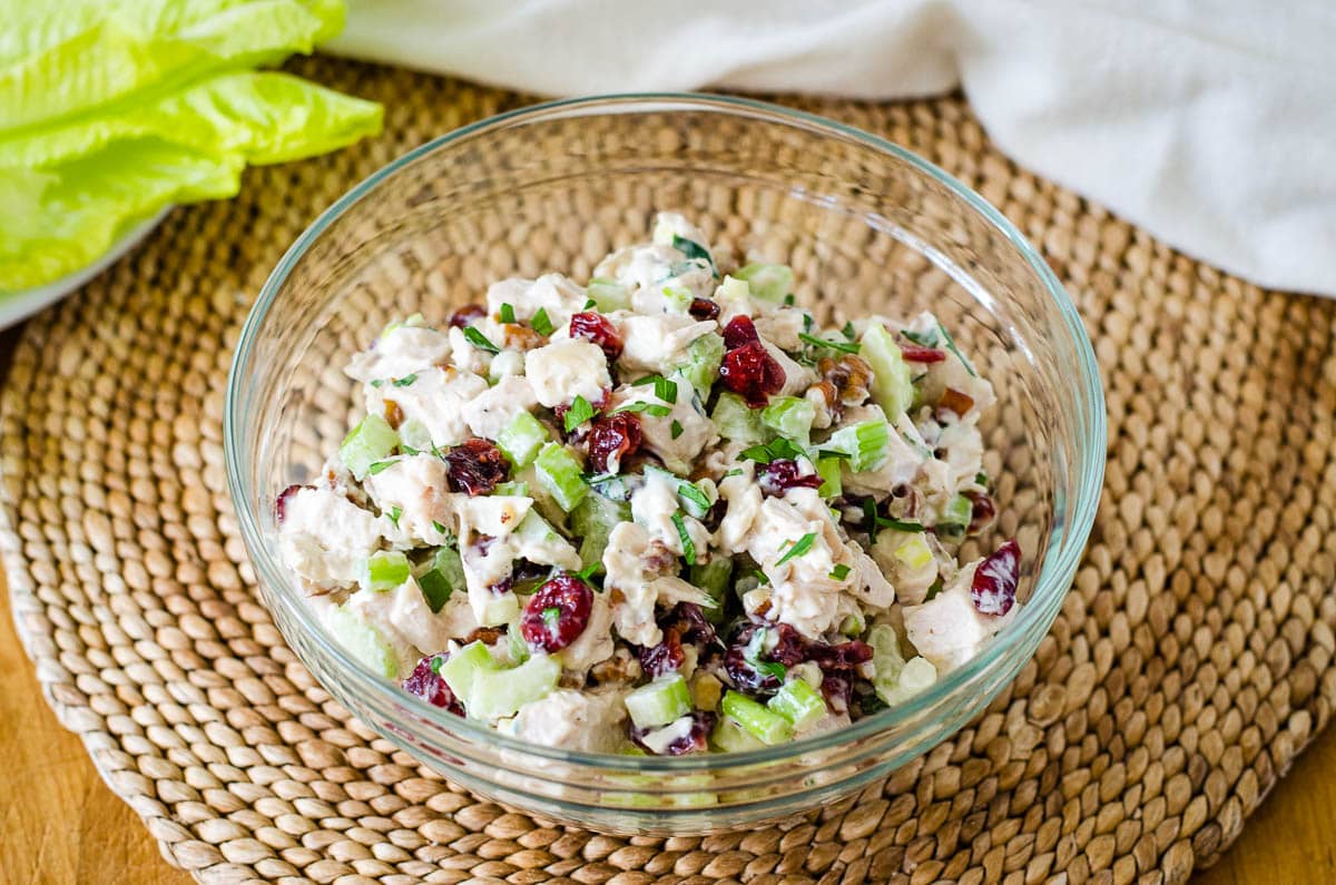 Turkey cranberry salad in glass bowl on placemat with lettuce and napkin in background.