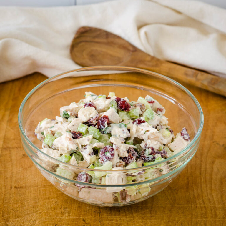 Turkey cranberry salad in glass bowl with wooden spoon and napkin in background.