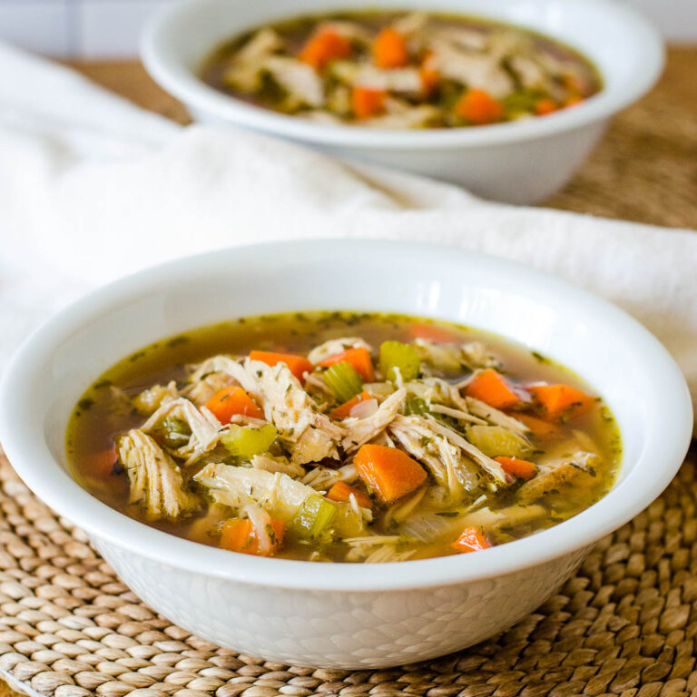 Leftover turkey soup in white bowl with napkin and another bowl in background.