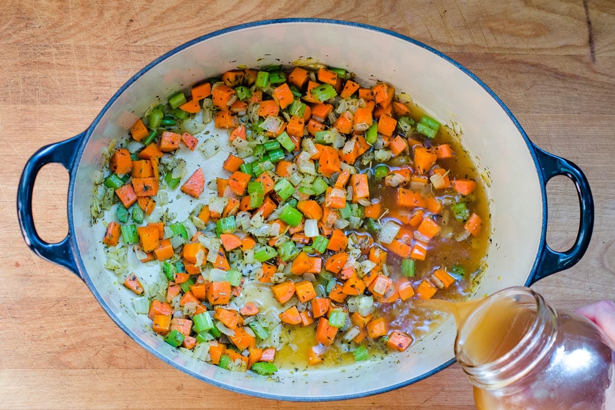 Pouring chicken broth into cooked veggies in Dutch oven.