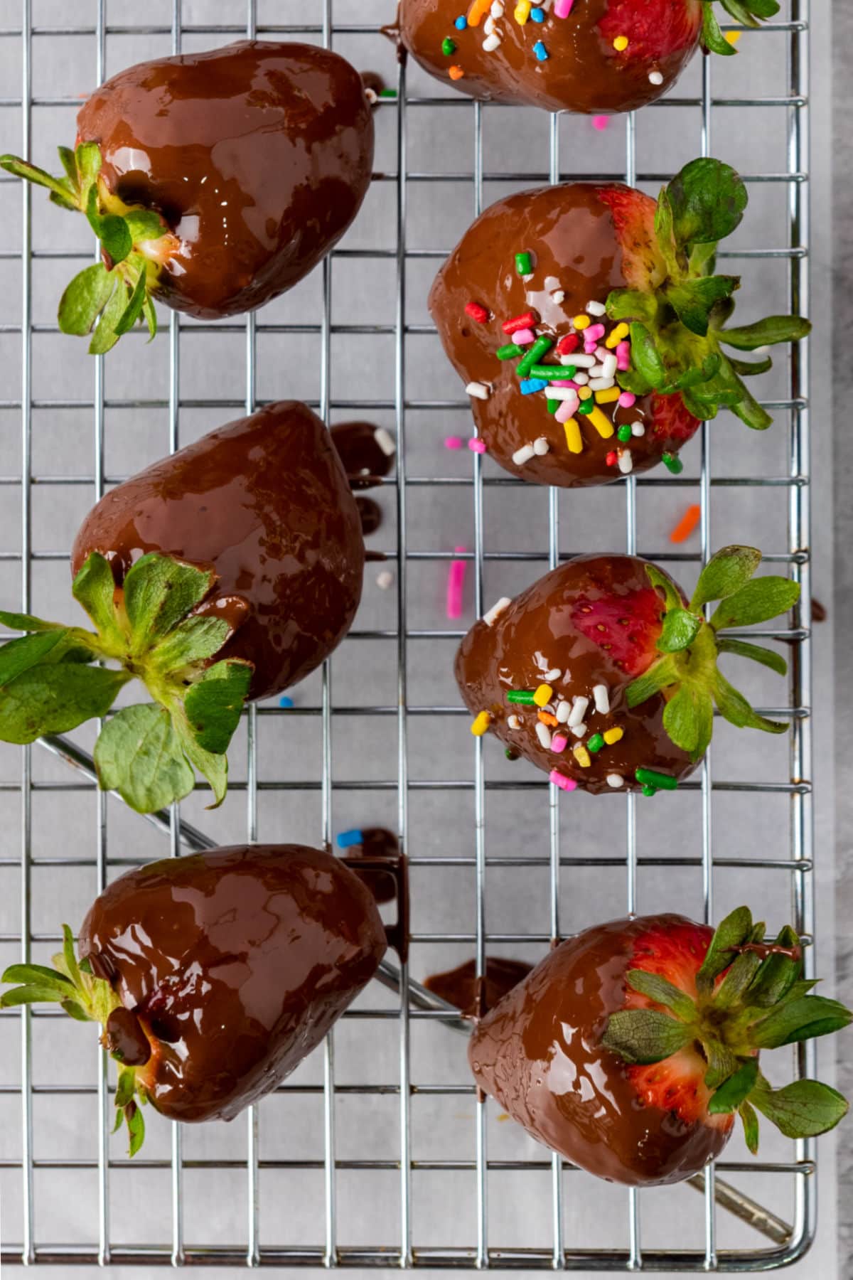 Chocolate dipped strawberries on wire rack, some with sprinkles.