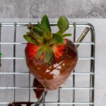 Chocolate dipped strawberry with leaves on a wire rack.