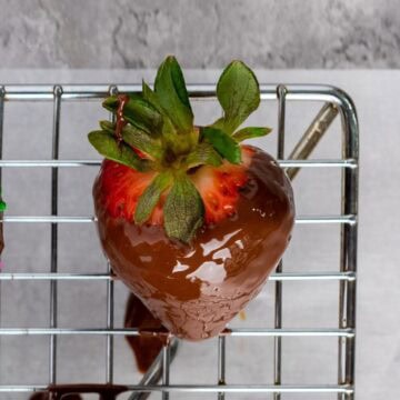 Chocolate dipped strawberry with leaves on a wire rack.