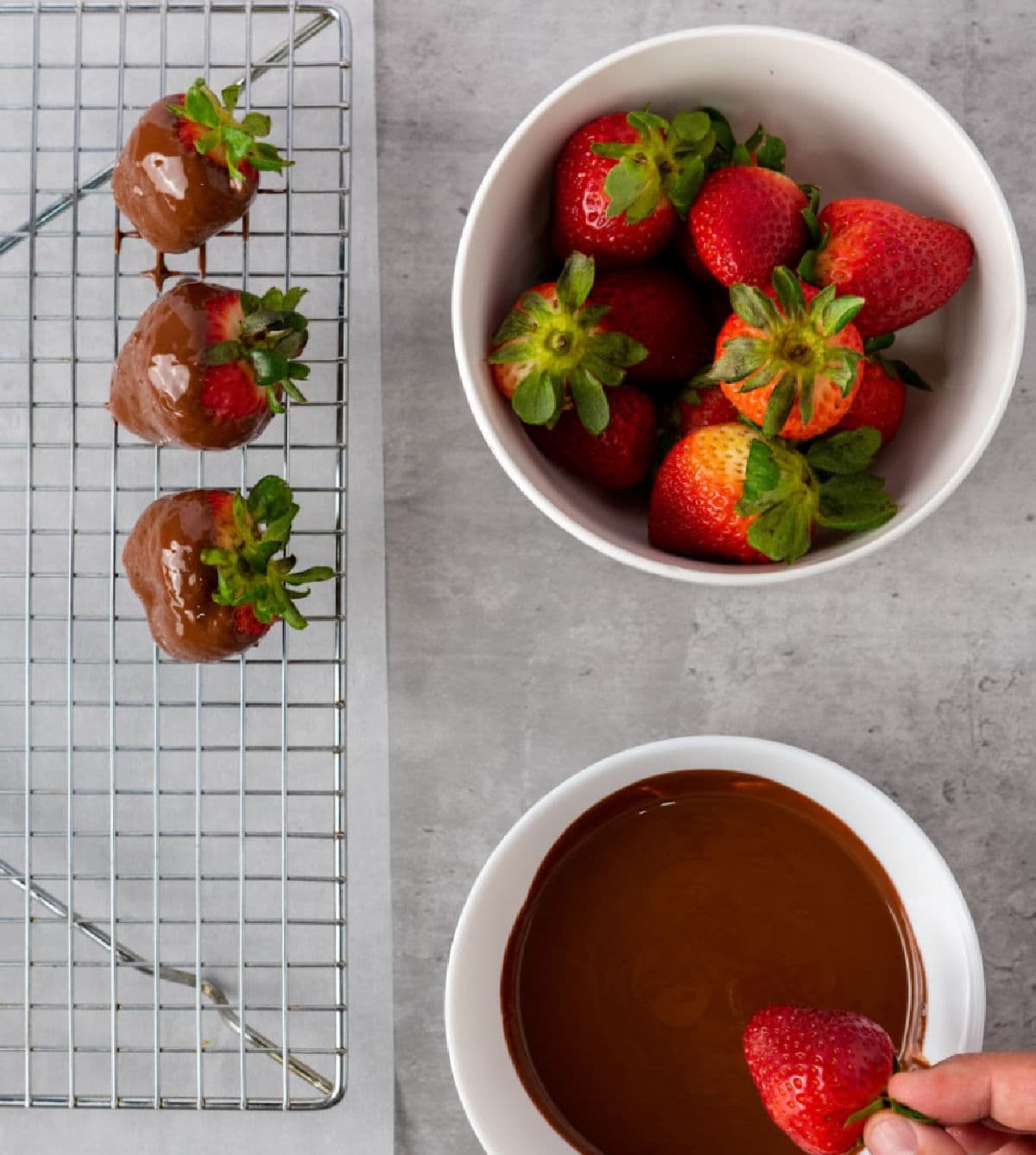 Chocolate dipped strawberries on wire rack next to bowls of strawberries and melted chocolate.
