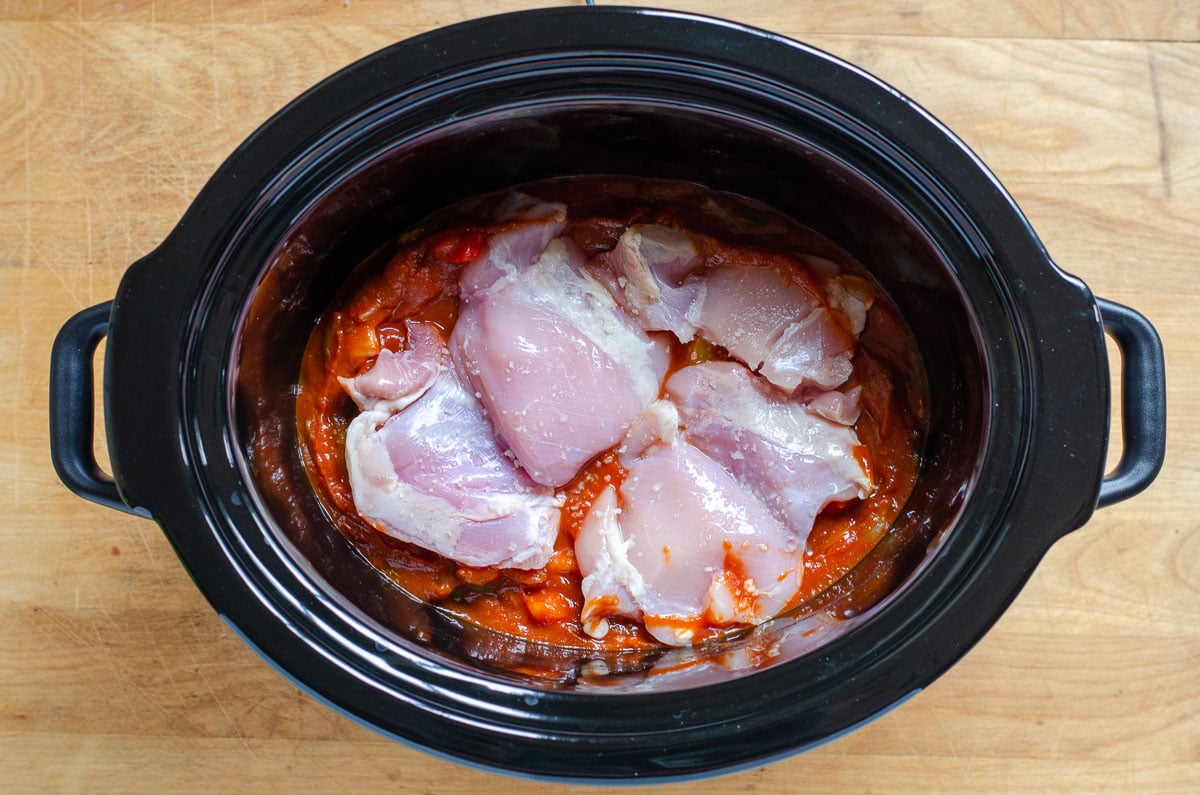 Boneless skinless chicken thighs on red sauce in crock pot.