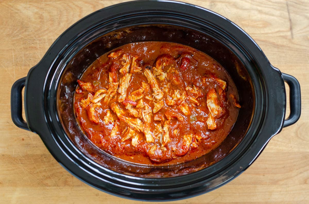 Shredded chicken in tomato sauce in slow cooker pot.