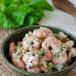 Cold shrimp salad in a green bowl on a natural placemat.