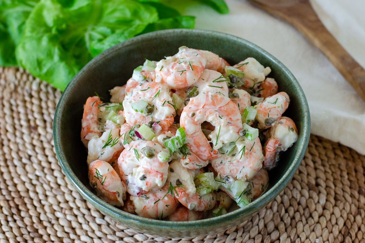 Bowl of shrimp salad with lettuce, napkin and wooden spoon in the background.