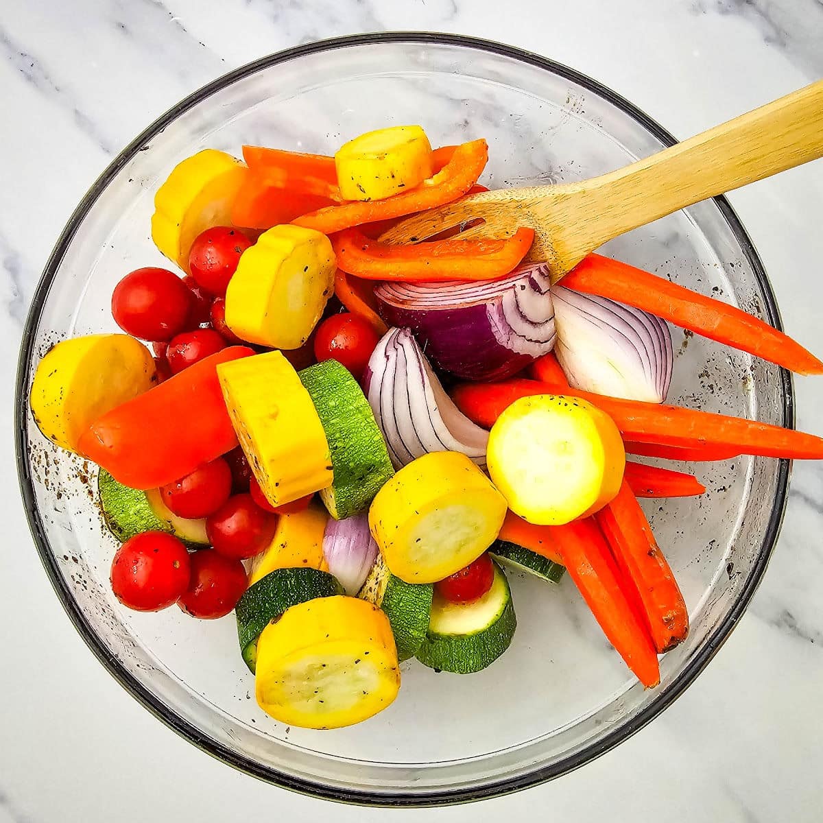 Cut vegetables in glass bowl with wooden spoon.