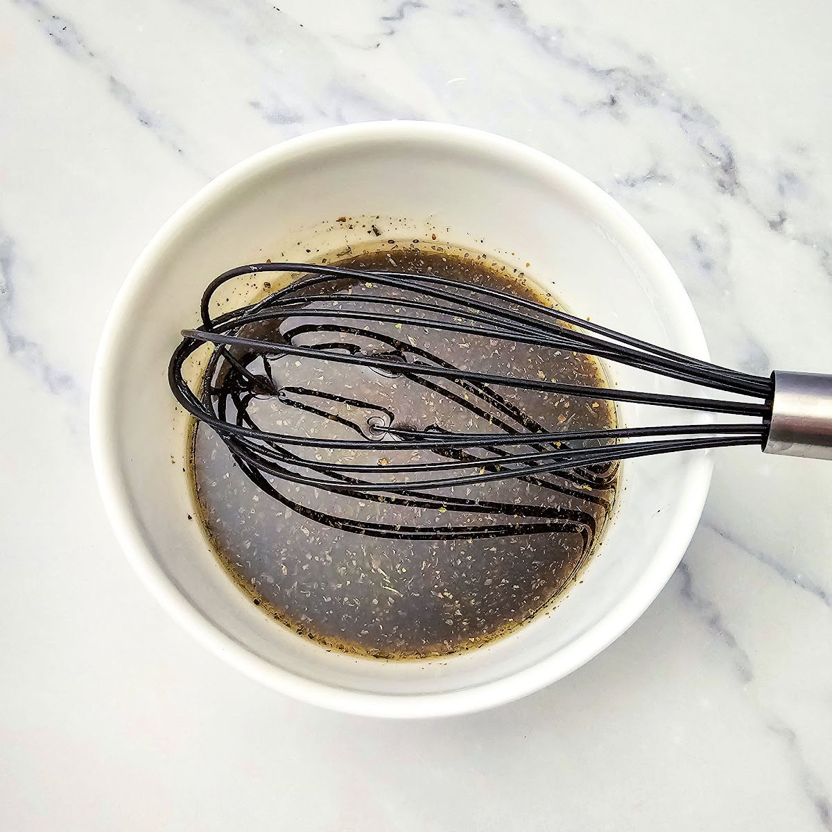 Whisking marinade in small white bowl.