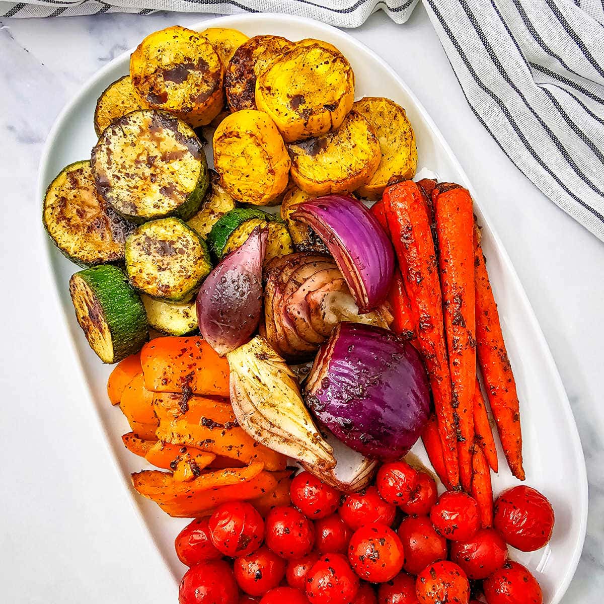 Grilled marinated vegetables on a white platter.