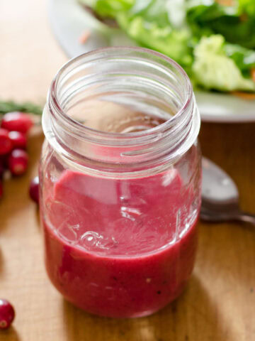 Cranberry salad dressing in mason jar next to cranberries, spoon and lettuce.