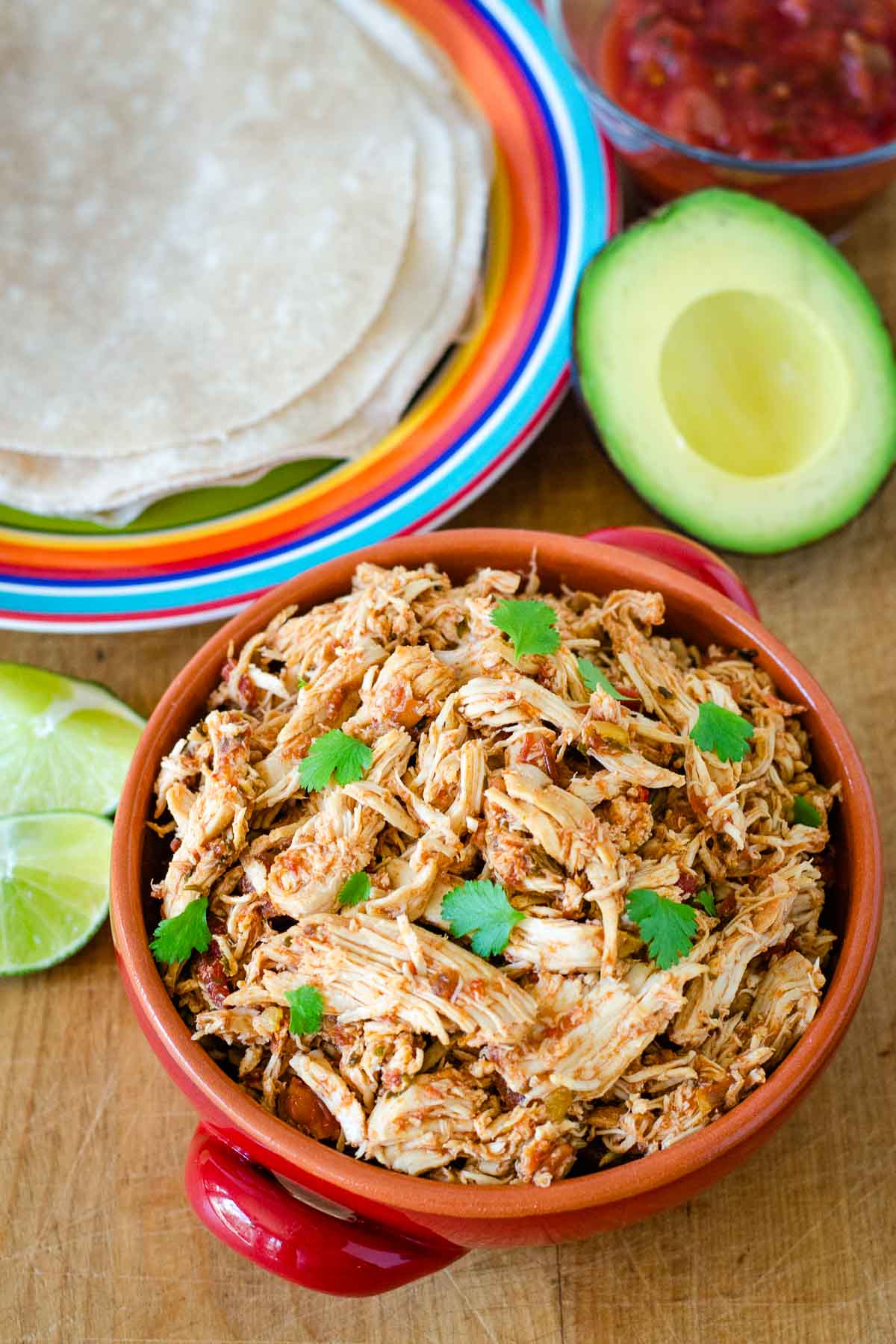 Bowl of shredded crockpot salsa chicken with tortillas, avocado and lime for tacos.