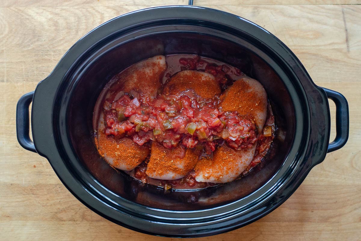Crock pot with chicken covered in spices and topped with salsa in the bottom.