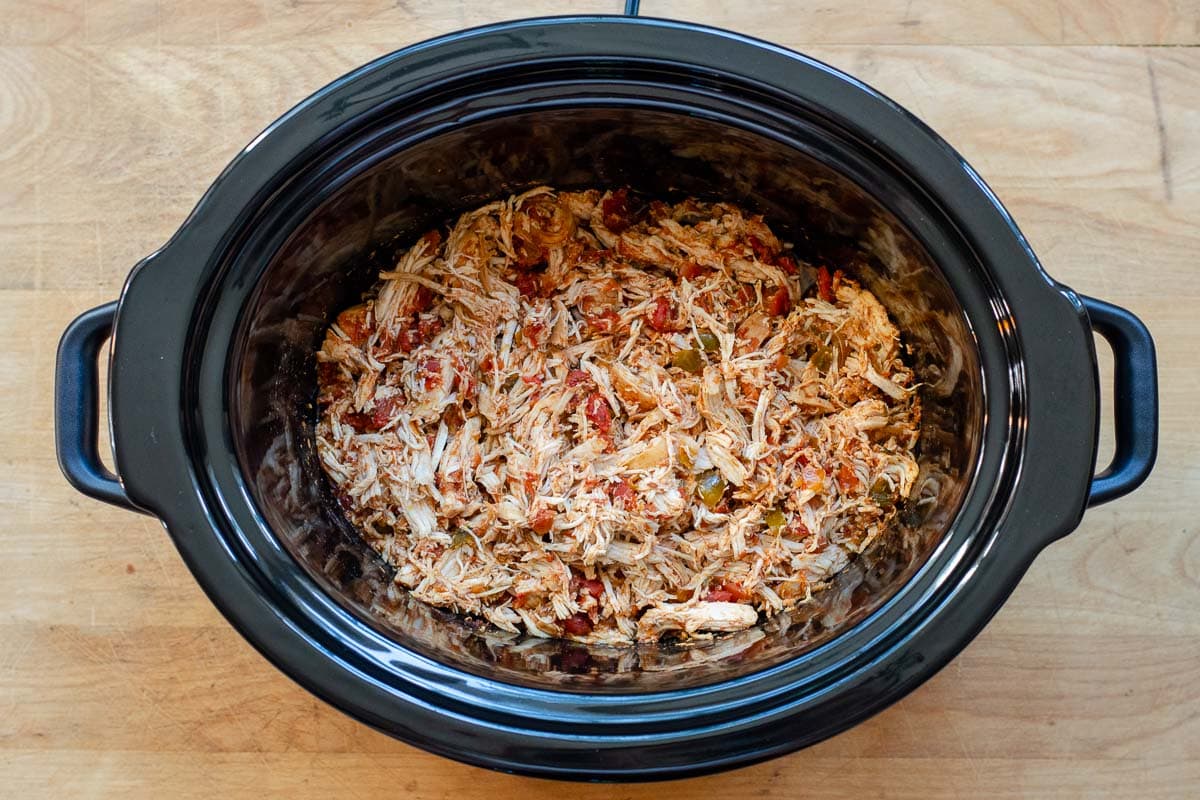 Crock pot with cooked shredded salsa chicken.