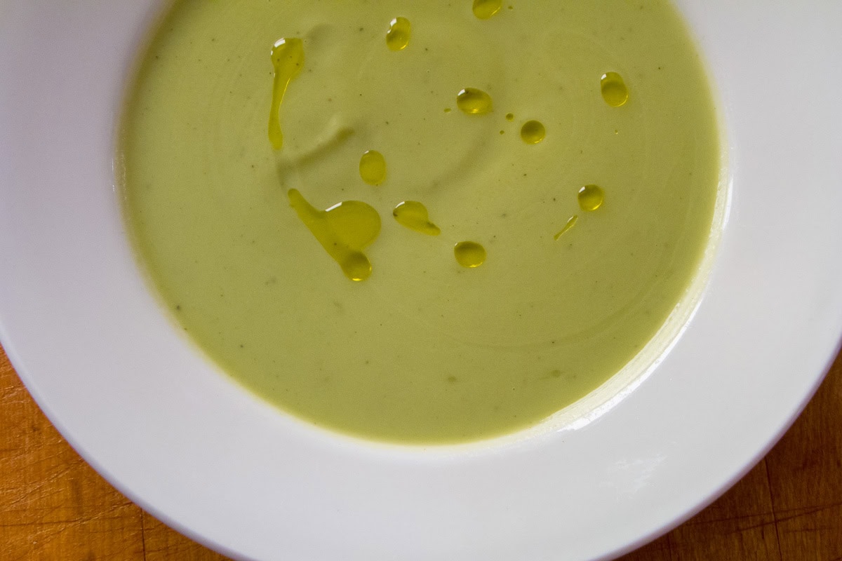Broccoli soup garnished with a drizzle of olive oil in a white bowl.