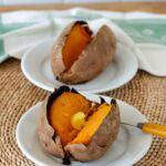 Baked sweet potato on a small white plate with another one in the background,