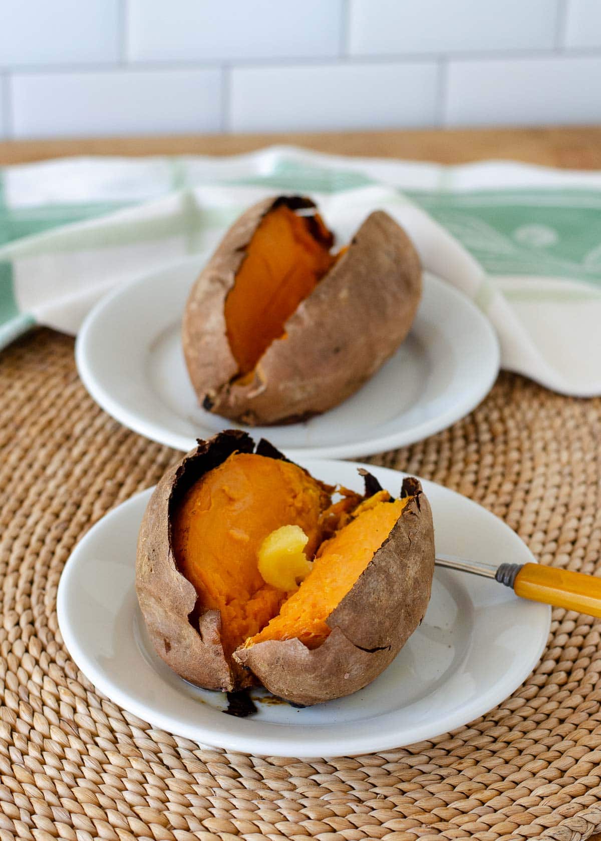 Baked sweet potato on a small white plate with another one in the background,