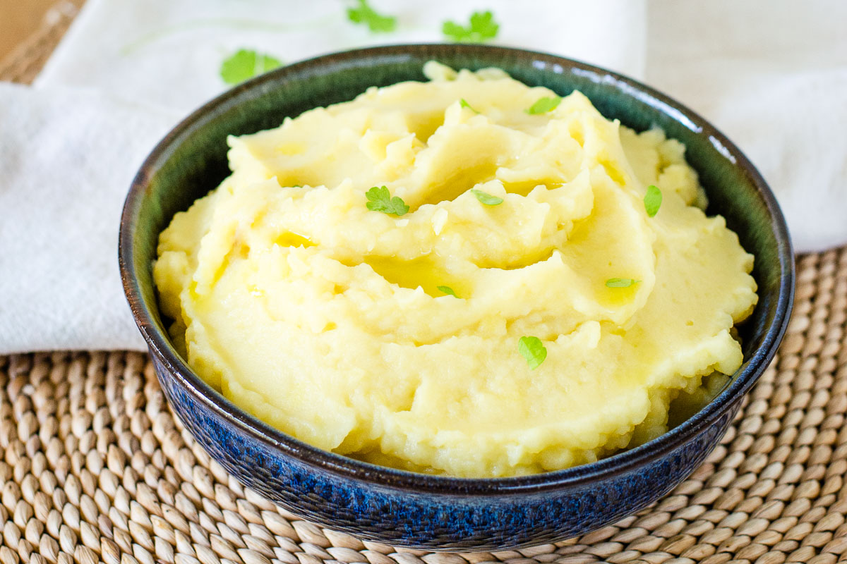 Creamy dairy-free mashed potatoes garnished with olive oil and parsley in a blue bowl.