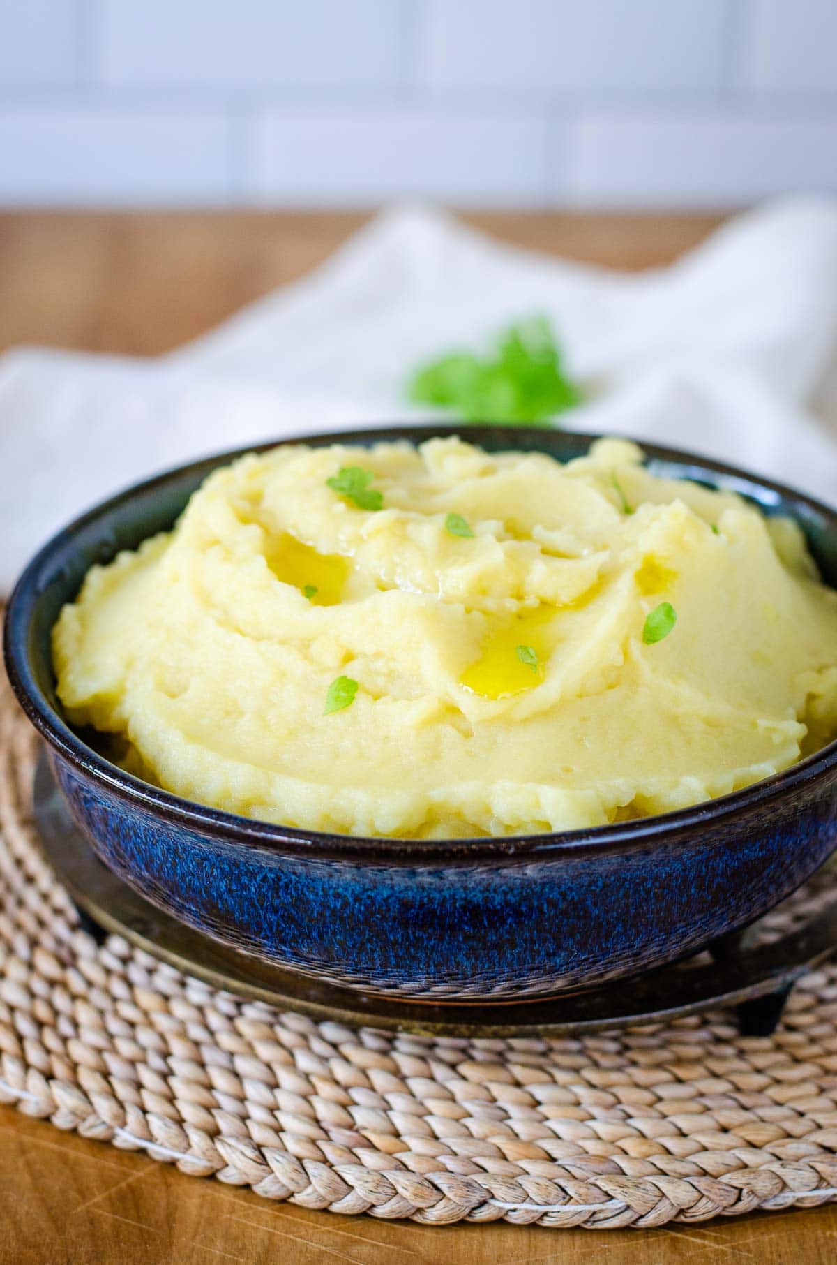 Dairy-free mashed potatoes garnished with olive oil and parsley in a bowl on a trivet.