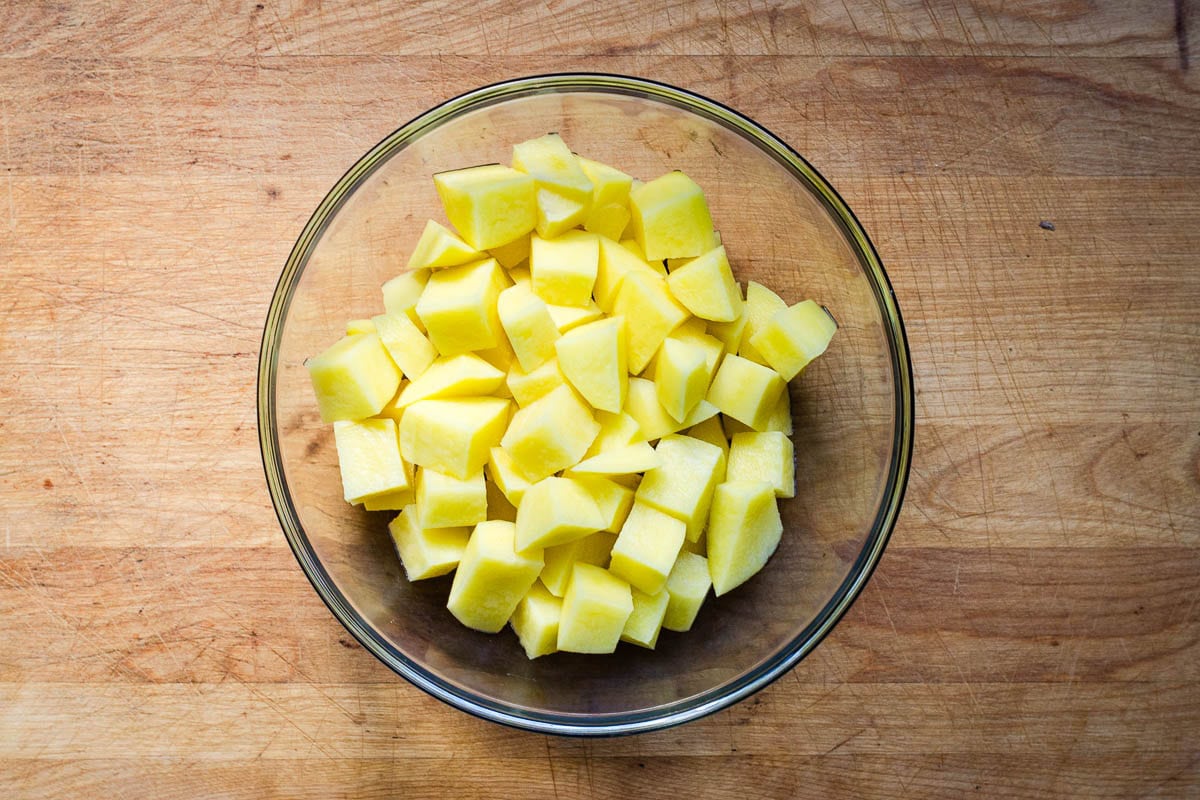 Large glass bowl with peeled and cubed raw potatoes.