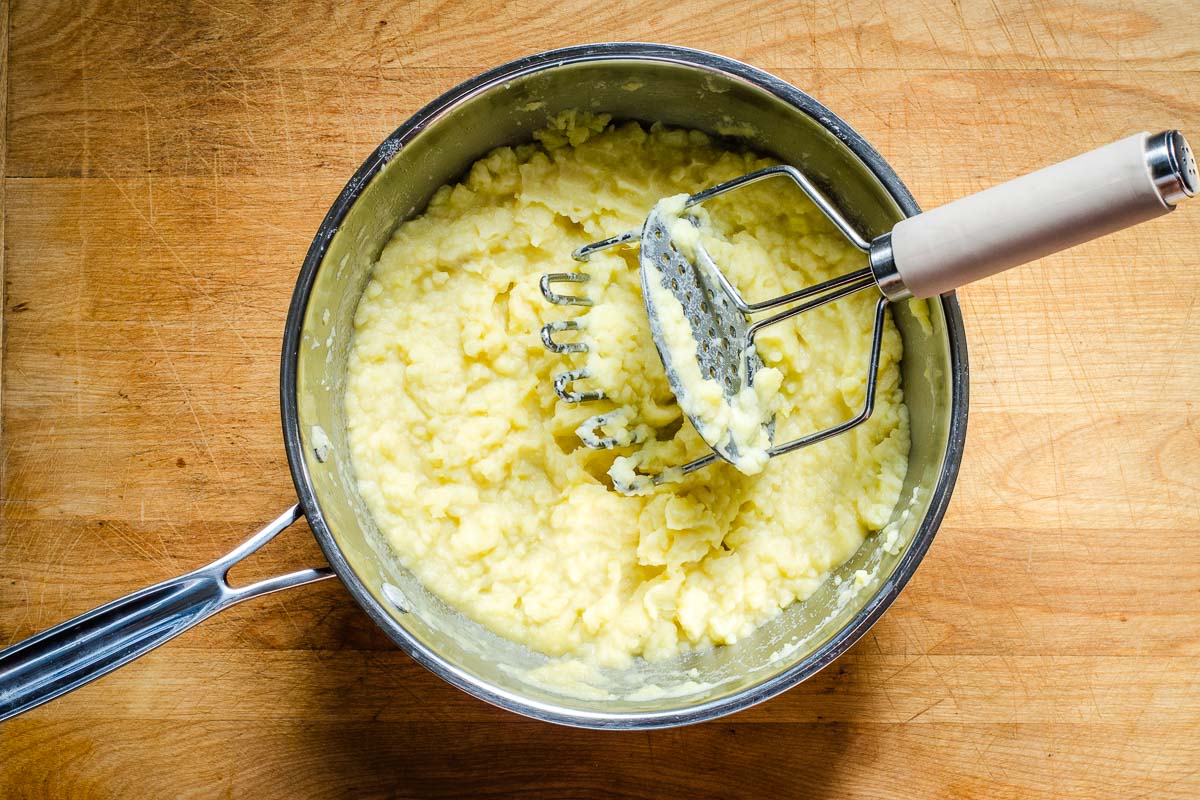 Saucepan with mashed potatoes and masher.