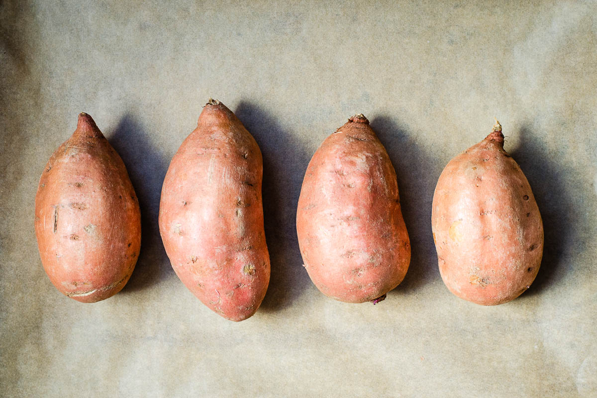 Four uncooked sweet potatoes on parchment paper.